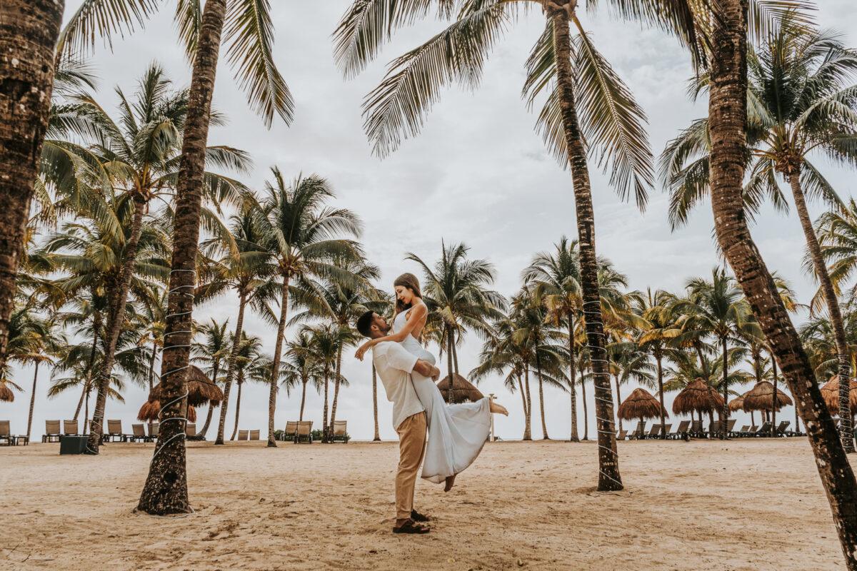 Romantic couple walking under palm trees during engagement session in Riviera Maya