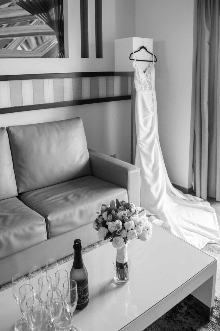 Black and white photo of a wedding dress hanging in a quiet bridal suite before a destination wedding in the Riviera Maya