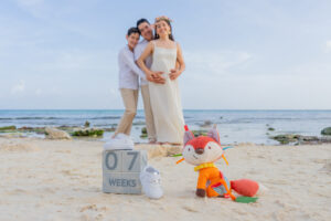 Expecting couple holding a baby ultrasound photo during a maternity session on the beach in Tulum, surrounded by ocean views