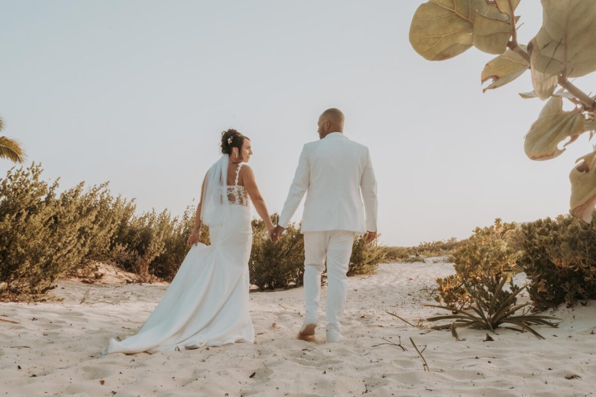 Bride and groom walking away together on the beach with wedding attire