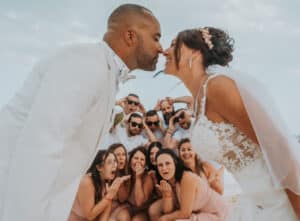 Bride and groom leaning in for a kiss with their bridal party cheering behind them – a playful wedding portrait photo perfect for wedding photos framed.